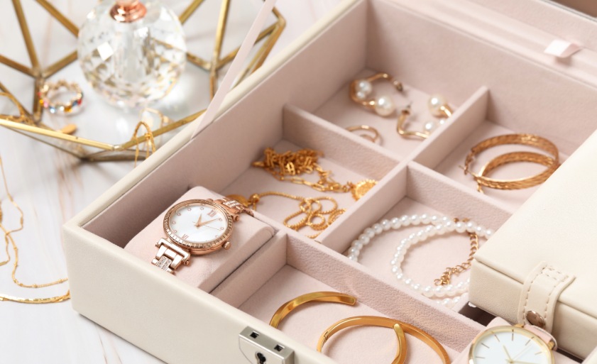 Jewelry box with many different accessories and perfume on white marble table, closeup