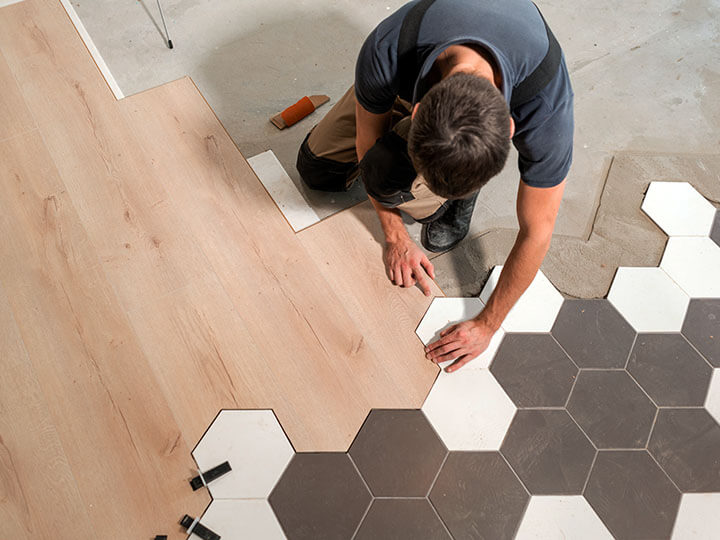 Male worker installing new flooring with a combination of wood panels and laminate and ceramic tiles in the form of honeycomb