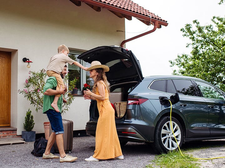 Father, Mother and Son loading luggage into trunk of electric car plugged into a charging station